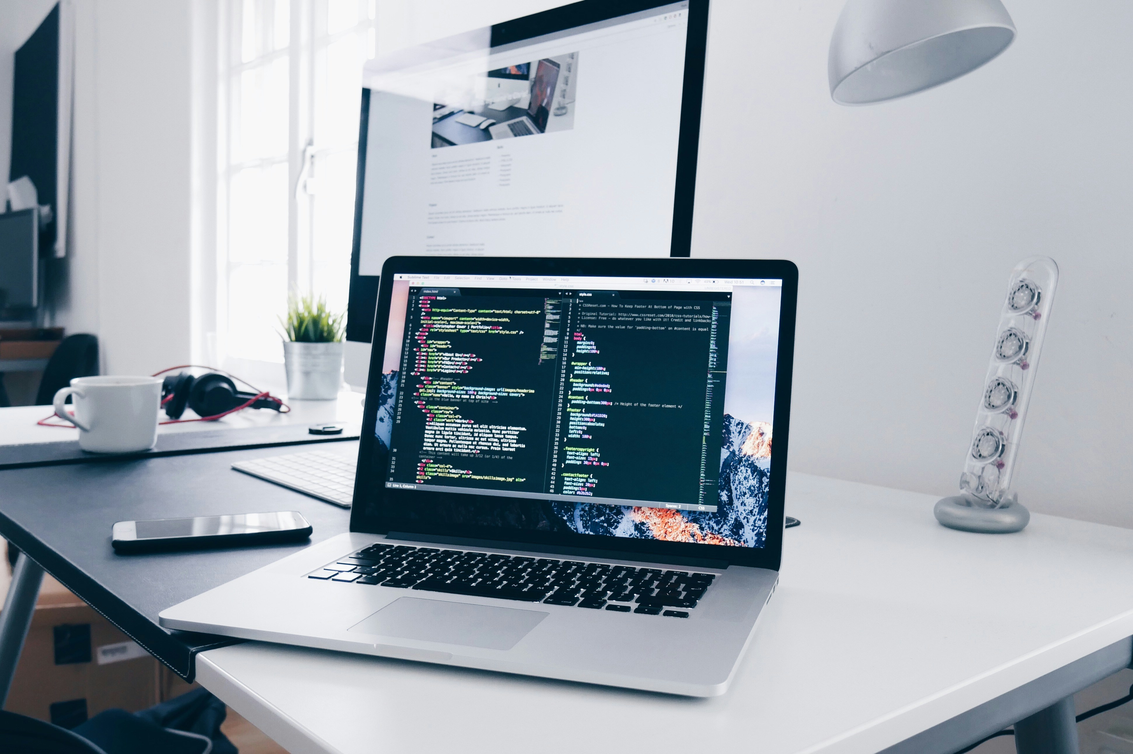 A clean developer workstation: a MacBook Pro with colorful syntax-highlighted code on a dark editor, surrounded by a minimalist desk setup